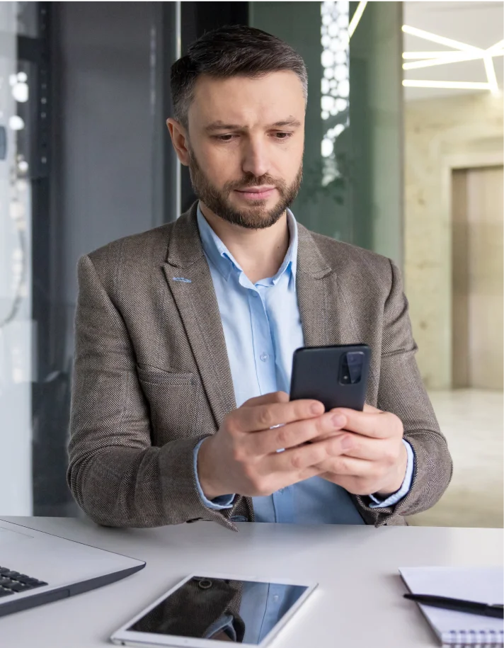 A man in a suit is intently looking at his phone, appearing focused on the screen.