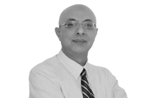 Bald man wearing glasses and a striped tie in a black and white portrait against a dark backdrop.
