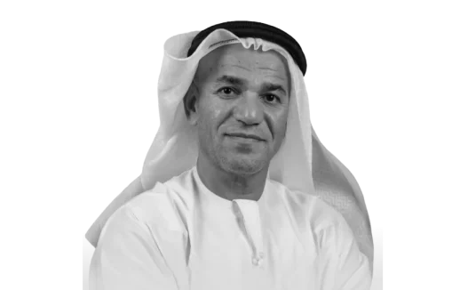 Black and white portrait of a smiling Middle Eastern man wearing a traditional white ghutra and agal headband.
