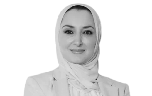 Monochrome portrait of a smiling woman wearing a hijab and a formal jacket.